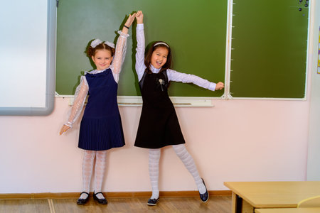 Educational concept. Two happy schoolgirls standing together by a schoolboard in a classroom.の写真素材