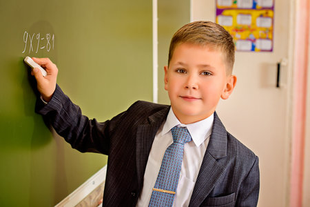 A schoolboy in uniform writing on a blackboard. Educational concept.