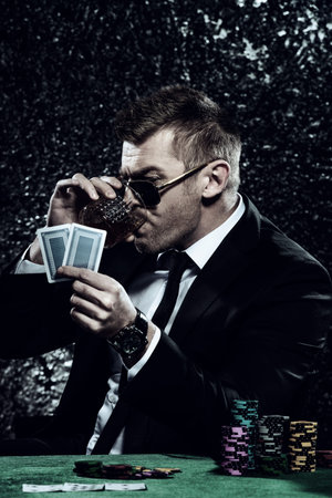 A wealthy mature man drinking brandy and playing poker with the excitement in a casino. Gambling,...