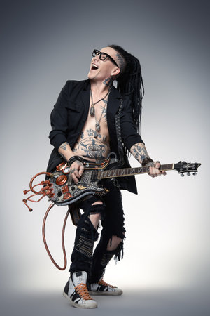 Excited rock musician is playing electrical guitar. Full length studio shot. Entertainment and...