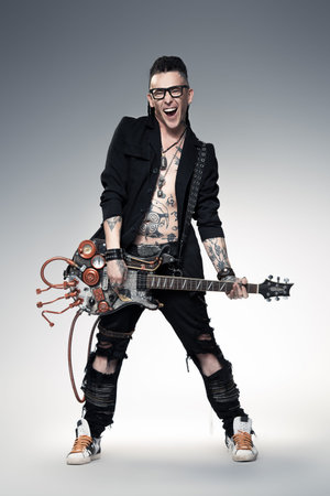 Excited rock musician is playing electrical guitar. Full length studio shot. Entertainment and...