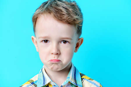 Portrait of a cute funny little boy looking at camera. Blue background. Copy space. Children fashion, summer concept.の写真素材
