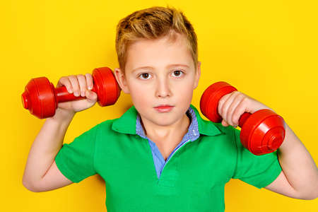 Portrait of a boy with dumbbells over yellow background. Healthy lifestyle. Sports and activities for children.の写真素材