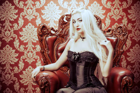 Gothic style. Beautiful young woman with long blonde hair and black make-up wearing long black dress. Vintage interior, castle style. Halloween.の写真素材