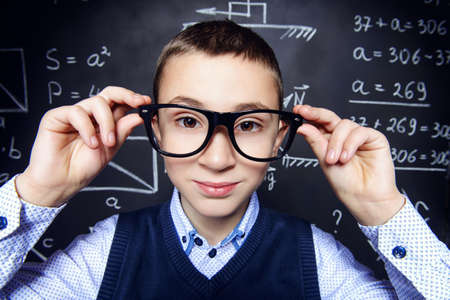 Funny smart boy in formal suit and glasses over school blackboard.の写真素材