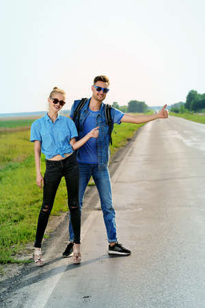 Hitchhiking couple. Happy young people standing on a highway.の写真素材