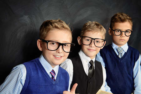Group of smart boys in formal suits and spectacles standing with books by a blackboard.の写真素材