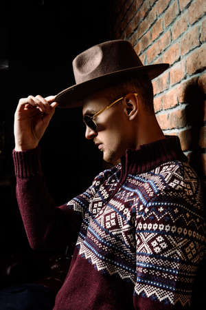 Portrait of a handsome man wearing sweater and hat standing by the brick wall.の写真素材
