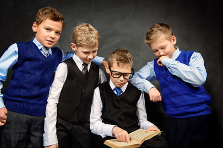 Group of smart boys in formal suits enthusiastically read the book by a blackboard.の写真素材