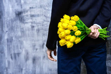 A man in elegant black suit hides a bouquet of tulips behind his back.の写真素材