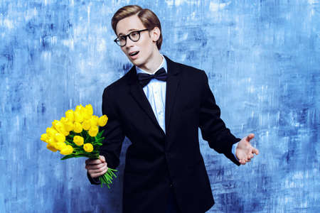 Excited handsome man in an elegant suit giving a bouquet of yellow tulips.の写真素材