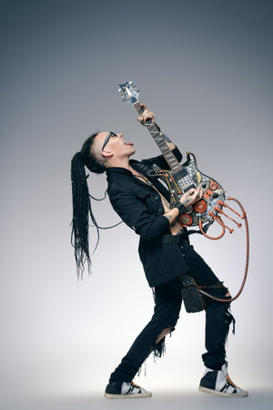 Stylish expressive rock musician is playing electrical guitar and shaking his hair. Full length studio shot. Entertainment and musical concept.の写真素材