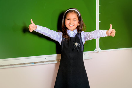 Portrait of a schoolgirl in uniform standing by a schoolboard in a classroom. Educational concept.の写真素材
