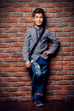 Kid's fashion. Modern nine year old boy posing at studio over brick wall background. Clothes and accessories for children.の写真素材