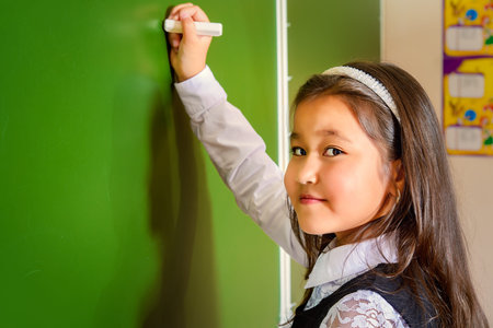 Portrait of a schoolgirl in uniform standing by a schoolboard in a classroom. Educational concept.の写真素材