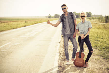 Hitchhiking couple. Romantic young people standing on a highway and catching a passing car.の写真素材