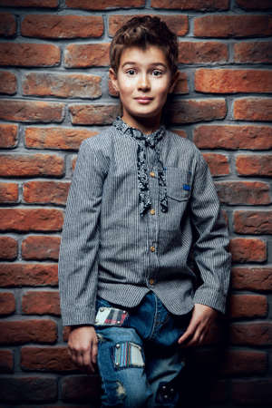 Kid's fashion. Modern nine year old boy posing at studio over brick wall background. Clothes for children.の写真素材
