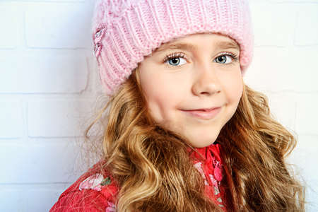 Winter clothes concept. Pretty smiling girl with long curly hair wearing pink knitted hat and smiling at camera.の写真素材