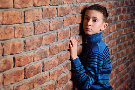 Portrait of a cute nine year old boy leaning against the brick wall.の写真素材