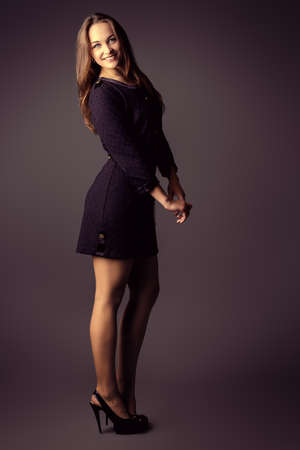 Full length portrait of a pretty young woman in black dress looking at camera and smiling. Studio shot.の写真素材