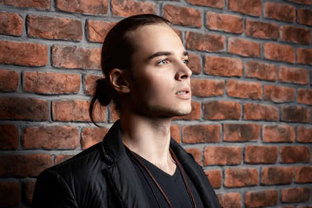 Fashion shot. Handsome sexual young man posing by the brick wall. Men's beauty.の写真素材