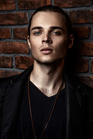 Fashion shot. Handsome sexual young man posing by the brick wall. Men's beauty.の写真素材