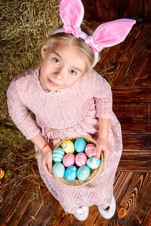 Easter holidays. Cute little girl in Easter Bunny costume holding colorful Easter eggs and smiling.の写真素材