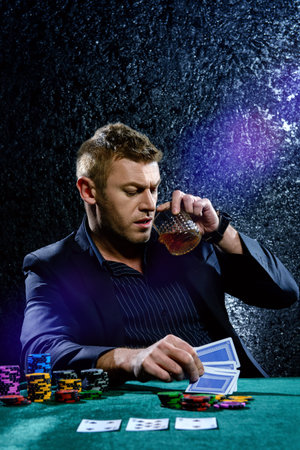 A wealthy mature man drinking brandy and playing poker with the excitement in a casino. Gambling, playing cards and roulette.の写真素材
