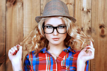 Pretty hipster girl in hat and glasses posing by a wooden wall. Youth style, fashion.の写真素材