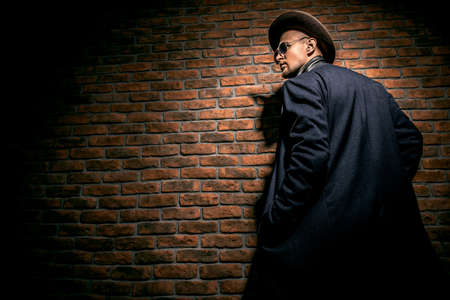Portrait of a stylish handsome man wearing hat, coat and sunglasses. Men's beauty, seasonal fashion. Brick wall background.の写真素材