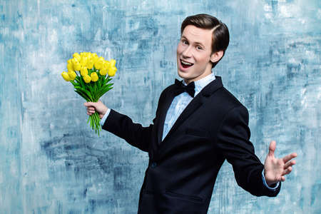 Excited handsome man in an elegant suit giving a bouquet of yellow tulips. Valentine's Day, Women's Day, Mother's Day. Wedding concept.の写真素材