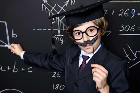 Smart schoolboy in black suit and glasses over school blackboard. Educational concept.の写真素材