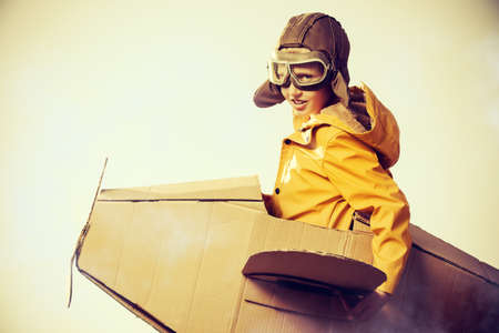 Eight-year boy playing with a cardboard airplane outdoor over sky background. Childhood. Fantasy, imagination.の写真素材
