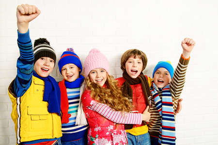 Group of happy joyful children standing together by a white brick wall. Kid's fashion. Warm clothing.の写真素材