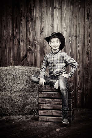 Portrait of a cute nine year old boy posing near the hay on the background of wooden wall. Western style, cowboy. Kid's fashion. Clothes for children.の写真素材