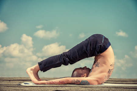 Yoga concept. Experienced yoga master performs various yoga poses on a roof over blue sky.の写真素材