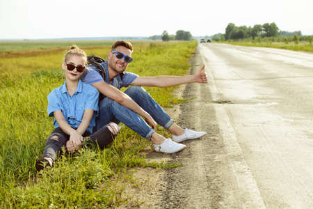 Hitchhiking couple. Happy young people sitting by the highway.の写真素材