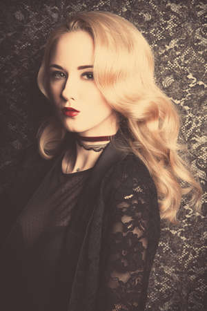 Gorgeous young woman with beautiful blonde hair posing over dark vintage background. Make-up, cosmetics. Evening and retro hairstyle.の写真素材
