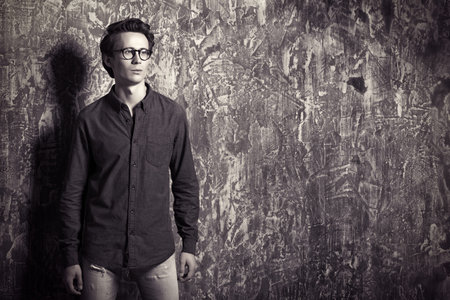 Portrait of young man in casual jeans clothes and spectacles posing over grunge background. Men's...