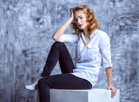 Fashion shot. Beautiful female model posing at studio in white shirt and black jeans. Youth style.の写真素材