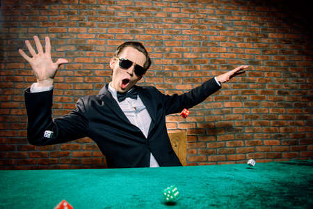 Excited gambling man throwing dice on a game table in a casino. Gambling, playing cards and roulette.の写真素材