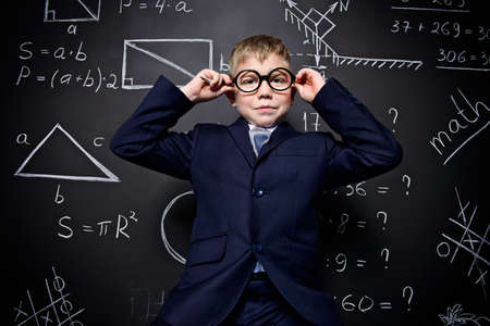 Smart schoolboy in black suit and glasses over school blackboard. Educational concept.の写真素材