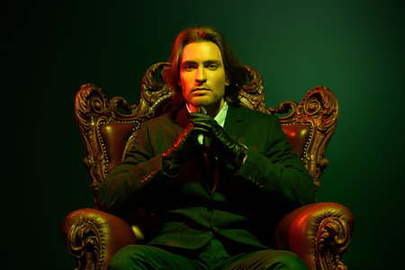 Handsome man in an expensive suit and black leather gloves sitting in a classical vintage armchair....