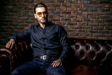 Portrait of a handsome young man in sunglasses over brick wall background. Men's beauty, fashion. Men's barbershop, Hairstyle.の写真素材
