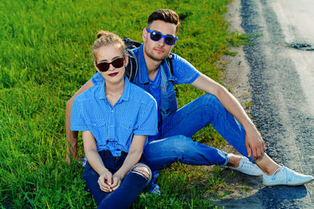 Hitchhiking couple. Happy young people sitting by the highway.の写真素材