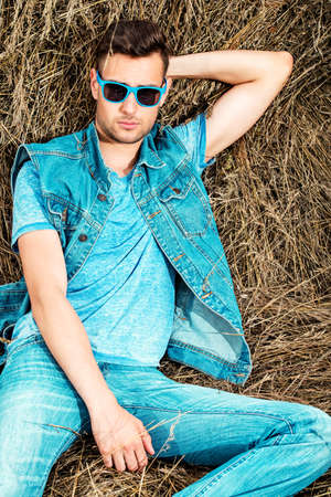 Handsome young man lying in haystack. Male fashion. Denim style.の写真素材