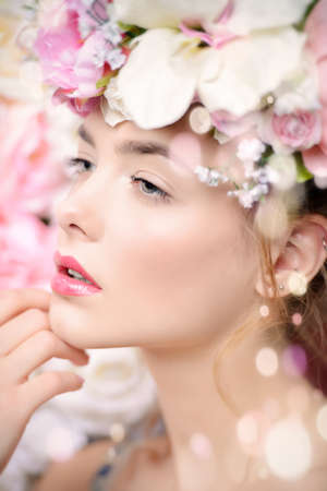 Beautiful romantic young woman in a wreath of flowers posing on a background of roses. Inspiration of spring and summer. Perfume, cosmetics concept.の写真素材