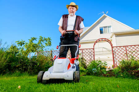 Happy retired senior man mows a lawn in his garden with a lawnmower.の写真素材