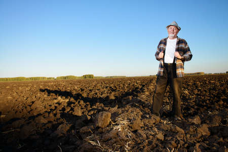 An elderly farmer standing in a plowed field. Agriculture, crop concept.の写真素材