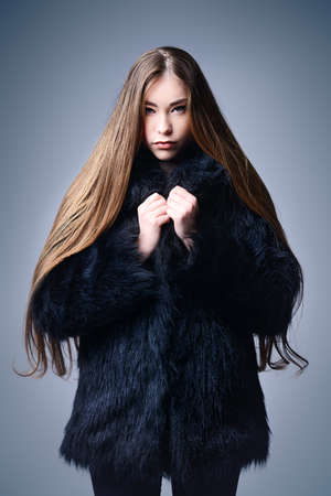 Fashion shot. Portrait of a fashionable model with beautiful long hair posing at studio in black fur coat.の写真素材